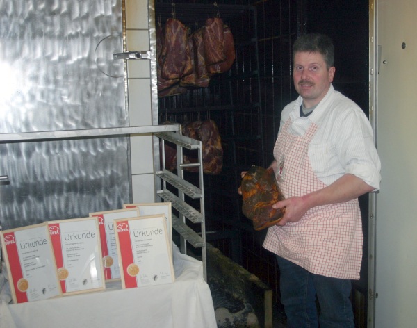Fleischermeister Edelbert Waßmer neben seinen Gold-Urkunden und mit einem Produkt aus seiner Produktion. Foto: Karl-Heinz Rümmele